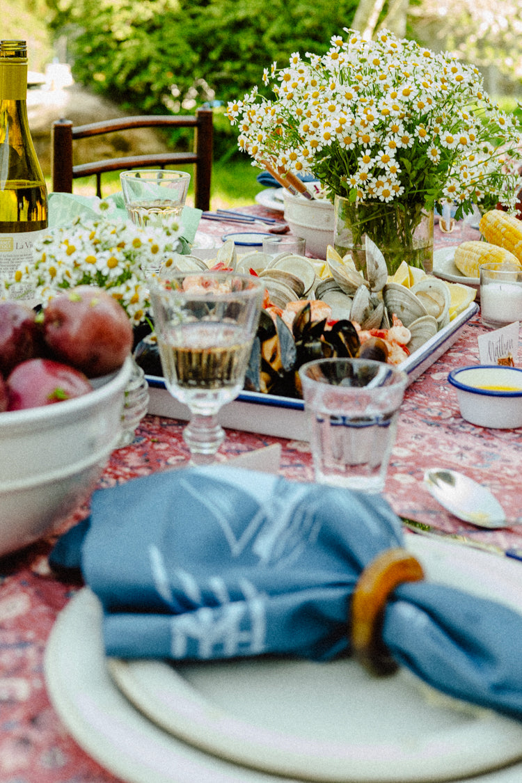 Close up of a summer table setting with a red tablecloth, a blue sailboat napkin, and blue silverware. 