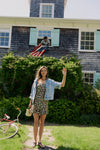 Woman standing in front of a house in a floral dress and jean jacket. 