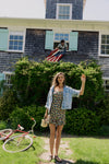 Woman standing in front of a house in a floral dress and jean jacket. 