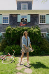 Woman standing in front of a house in a floral dress and jean jacket. 