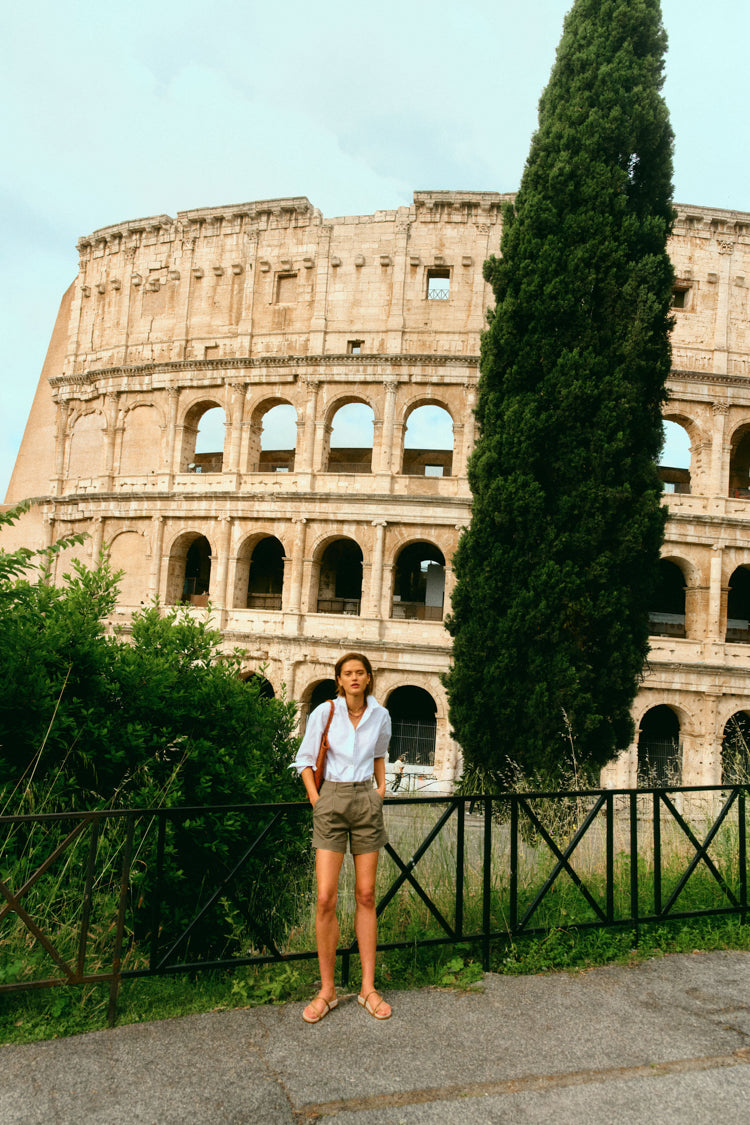 Woman standing in front of the Colosseum in a white button down and olive shorts. 
