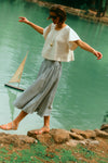 Woman walking on the edge of water in a white top and a stripe skirt. 