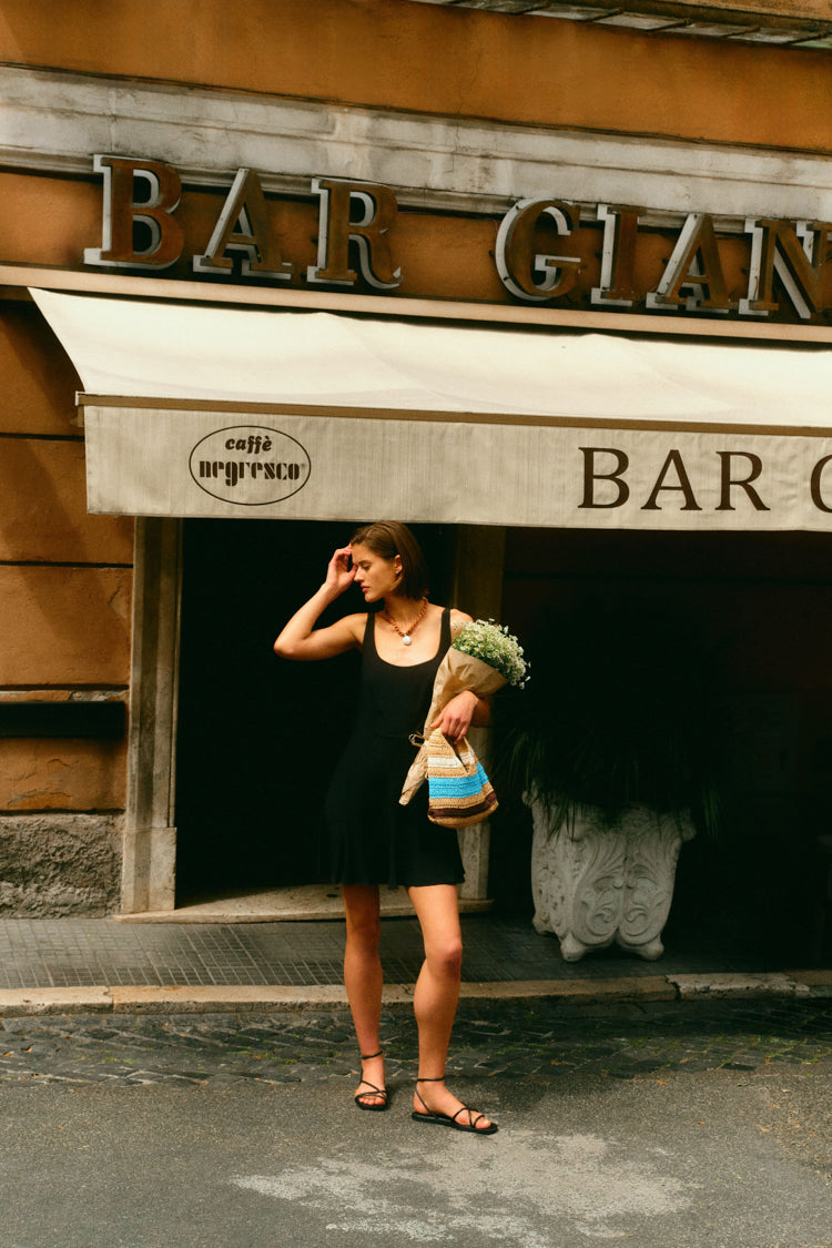 Woman standing in front of a bar in a little black dress and holding a bouquet of flowers. 