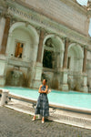 Woman standing by a fountain in a navy embroidered dress. 