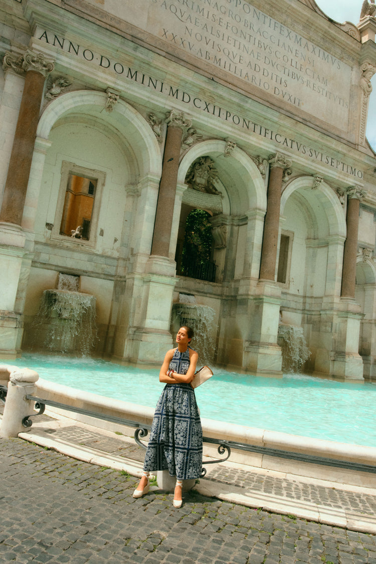 Woman standing by a fountain in a navy embroidered dress. 