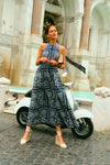Woman standing in front of a vespa and fountain in a navy embroidered halter dress. 