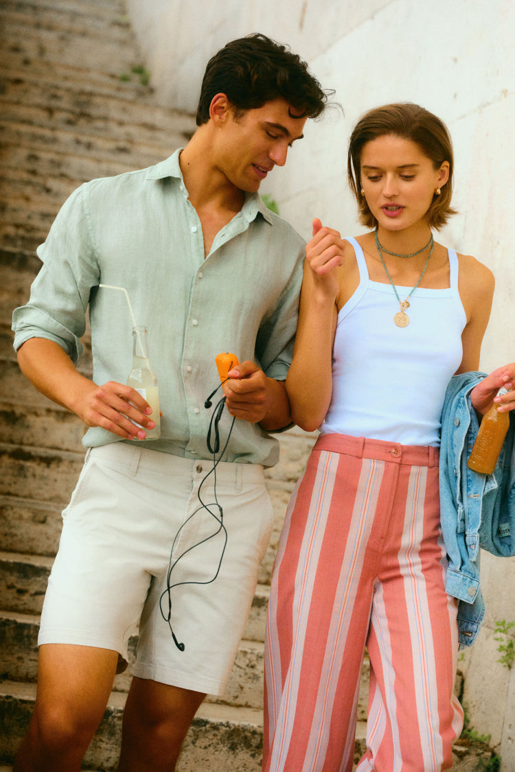 Man and woman walking together down the stairs. Woman is in a white tank and red and white striped pants. 