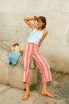 Woman leaning on a stone structure in a white tank and red and white striped pants. 