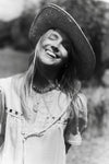 Black and white image of a woman in a field in a linen dress and a straw hat. 