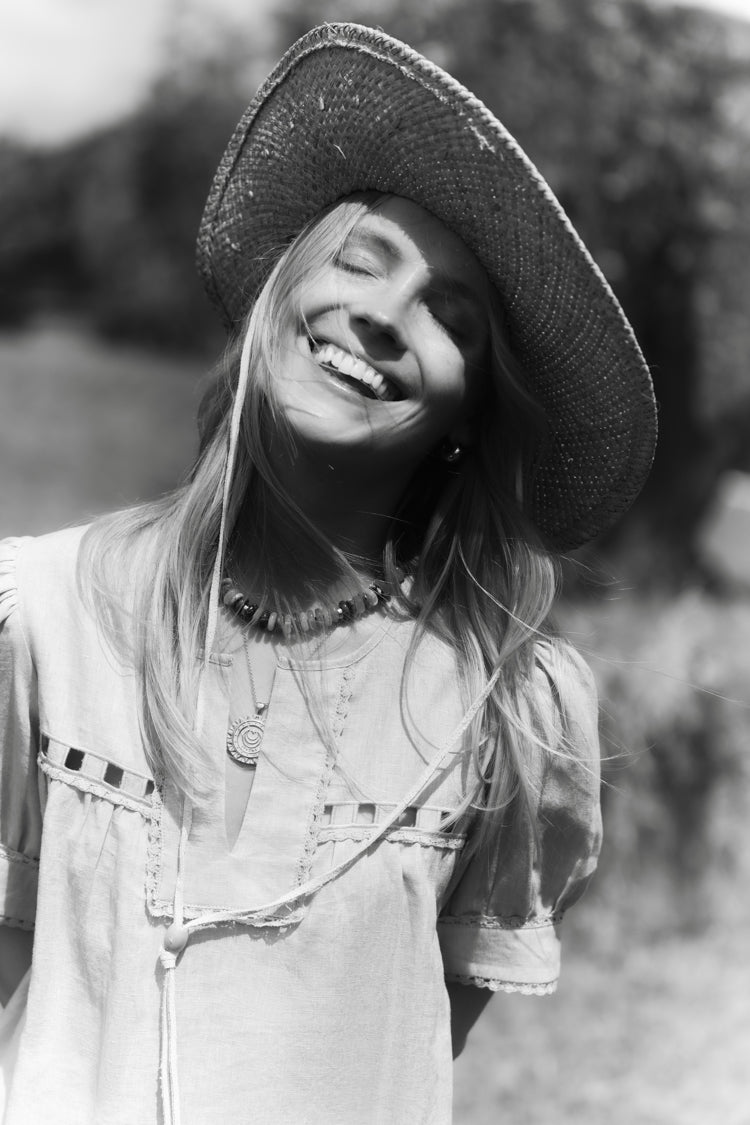 Black and white image of a woman in a field in a linen dress and a straw hat. 