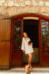 Woman standing in a wooden doorway in a white dress with a dachshund.  