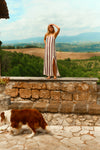 Woman standing on a wall overlooking the Tuscan countryside in a brown and white striped dress. 