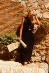 Woman standing in front of a brick and stone wall in a black dress. 