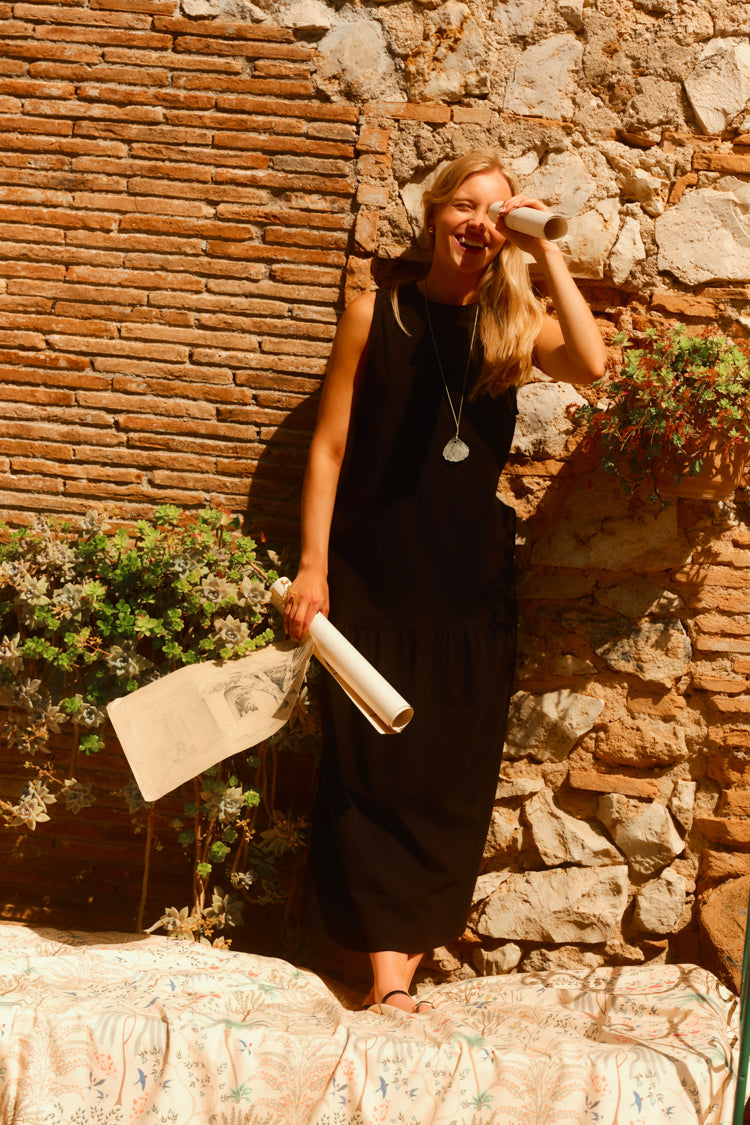 Woman standing in front of a brick and stone wall in a black dress. 