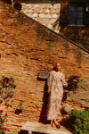 Woman standing in front of a brick wall in a brown and white patterned dress. 