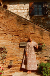 Woman standing against a brick wall in a brown and white printed maxi dress. 