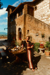 Woman leaning on a table outside of a Tuscan villa in a black and red printed caftan. 
