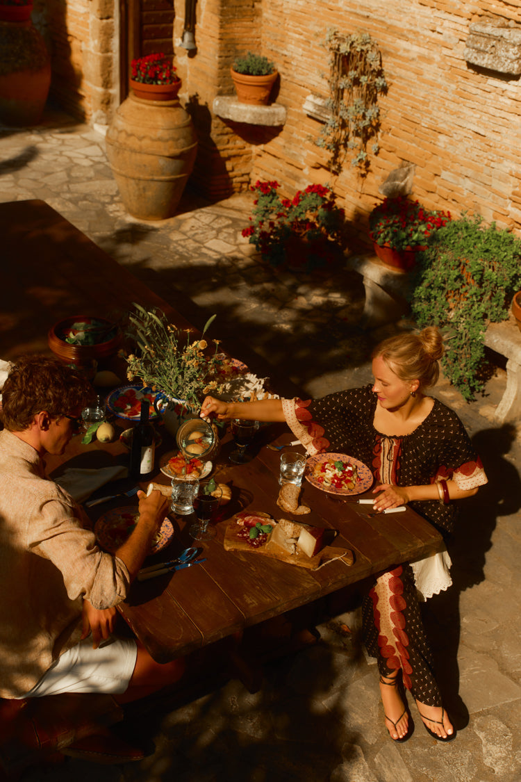 Woman sitting at a table outside of a Tuscan villa in a black and red printed caftan. 