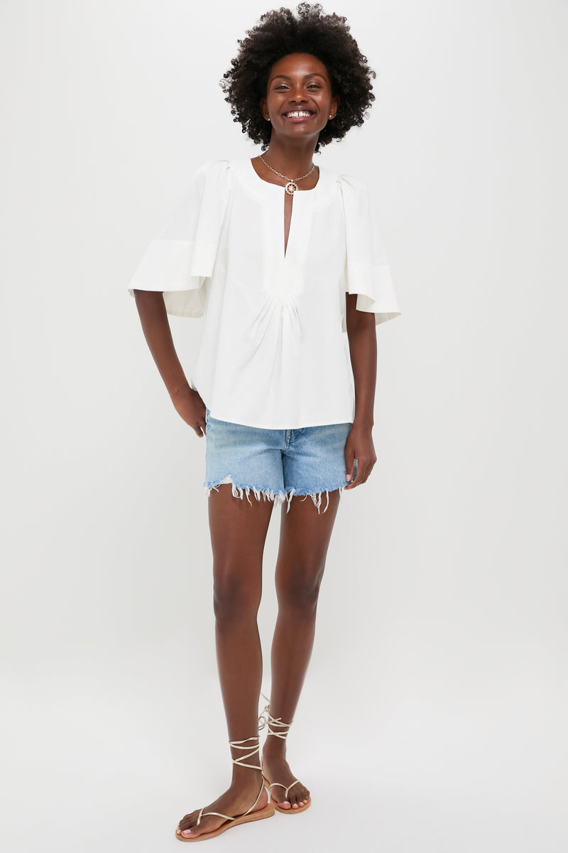 A person stands against a plain background wearing a Pomander Place 100% cotton white V-neck flutter sleeve top, light blue frayed denim shorts, and brown strappy sandals.