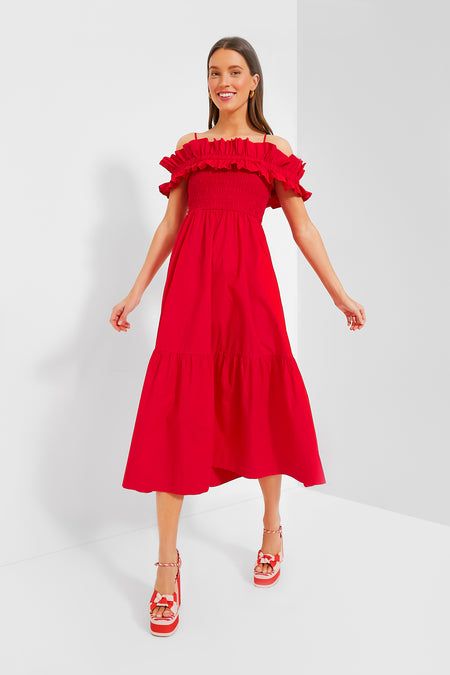 A woman in a vibrant red off-the-shoulder GANNI dress and coordinating red platform sandals stands in a minimalist white room.