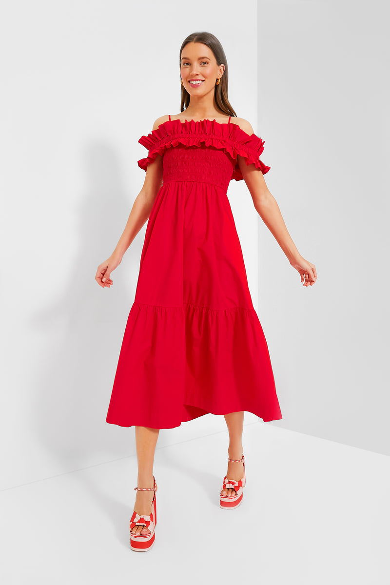 A woman in a vibrant red off-the-shoulder GANNI dress and coordinating red platform sandals stands in a minimalist white room.