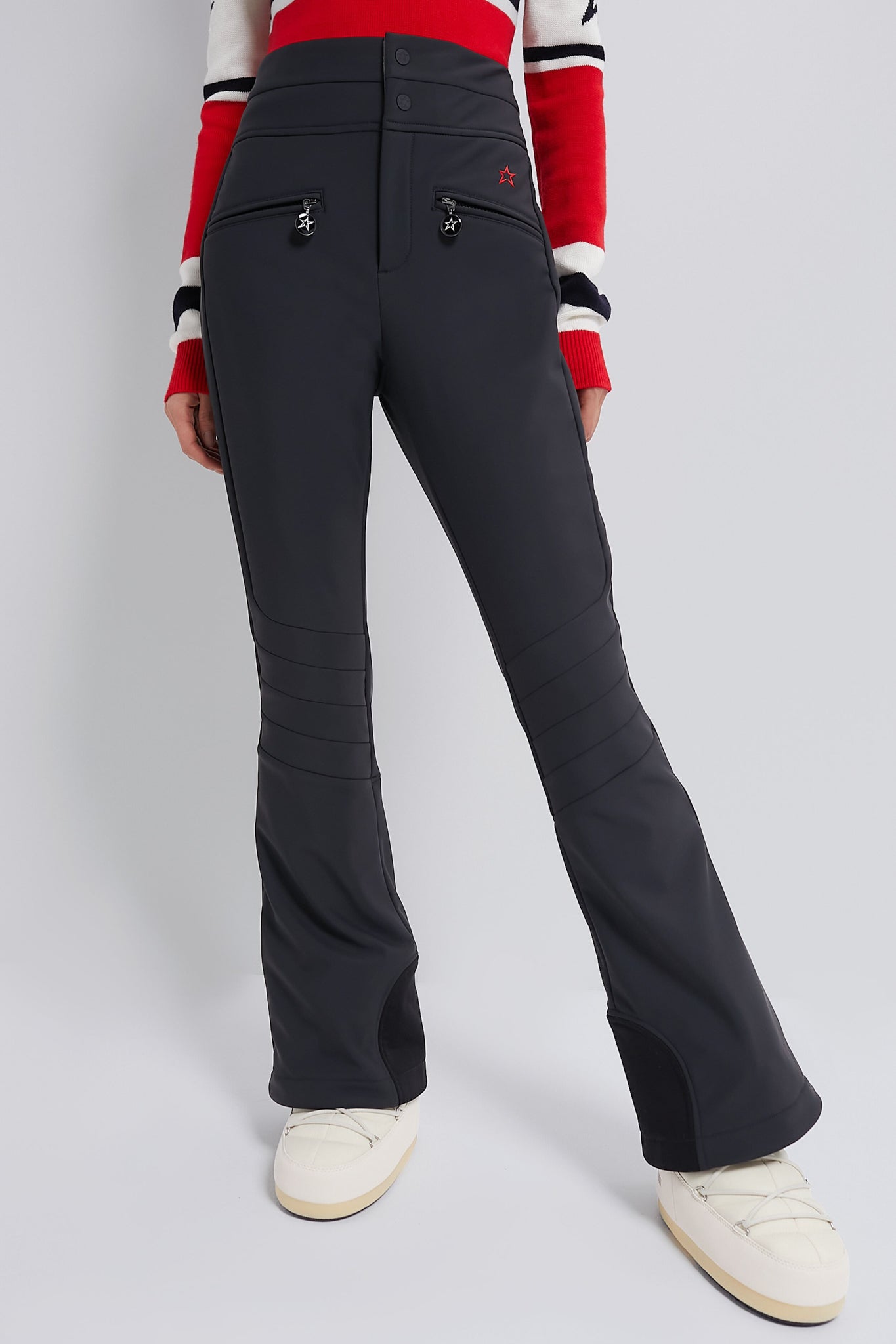 Black Aurora High Waist Ski Pant with classic, effortless fit and fun star-shaped zipper charms, modeled with off-white snow boots and striped sweater hem.