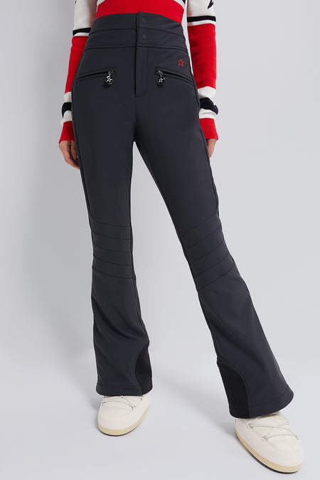 Black Aurora High Waist Ski Pant with classic, effortless fit and fun star-shaped zipper charms, modeled with off-white snow boots and striped sweater hem.