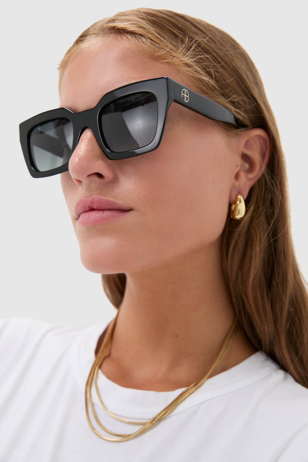 Model wearing Black Indio Sunglasses with oversized square frames, drop gold earrings, and necklaces, showcasing a classic, effortless, high-end style perfect for everyday confidence.