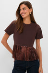 A woman wears a Hyacinth House Francie blouse, a short-sleeve brown party top featuring metallic fringe at the hem, styled with dark jeans.