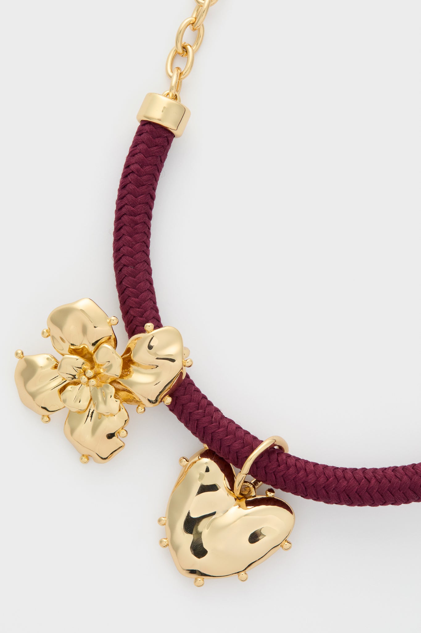 Maroon Lelani Necklace featuring a classic maroon braided cord, removable gold heart and flower charms, offering an effortless, fun, high-end accessory perfect for versatile styling.