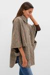 Young woman in profile wearing the Herringbone Stewart Poncho with classic herringbone pattern, stand-up collar, and oversized pockets, creating an effortless, high-end look.