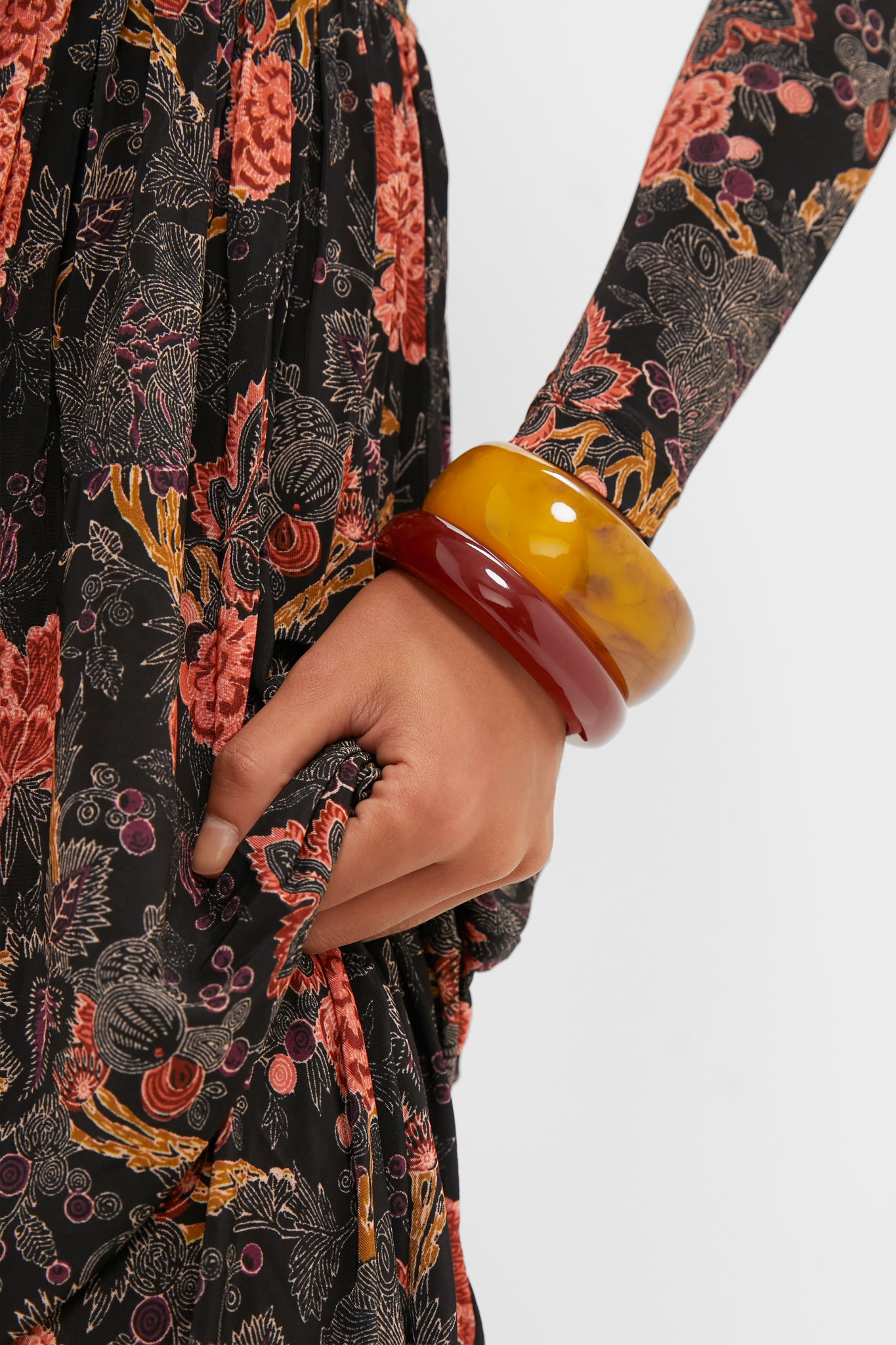 Close-up of the Oxblood and Tortoise Rita Bangle Set, featuring two chunky resin bangles on a wrist, adding classic, effortless flair to a vintage-style floral dress.