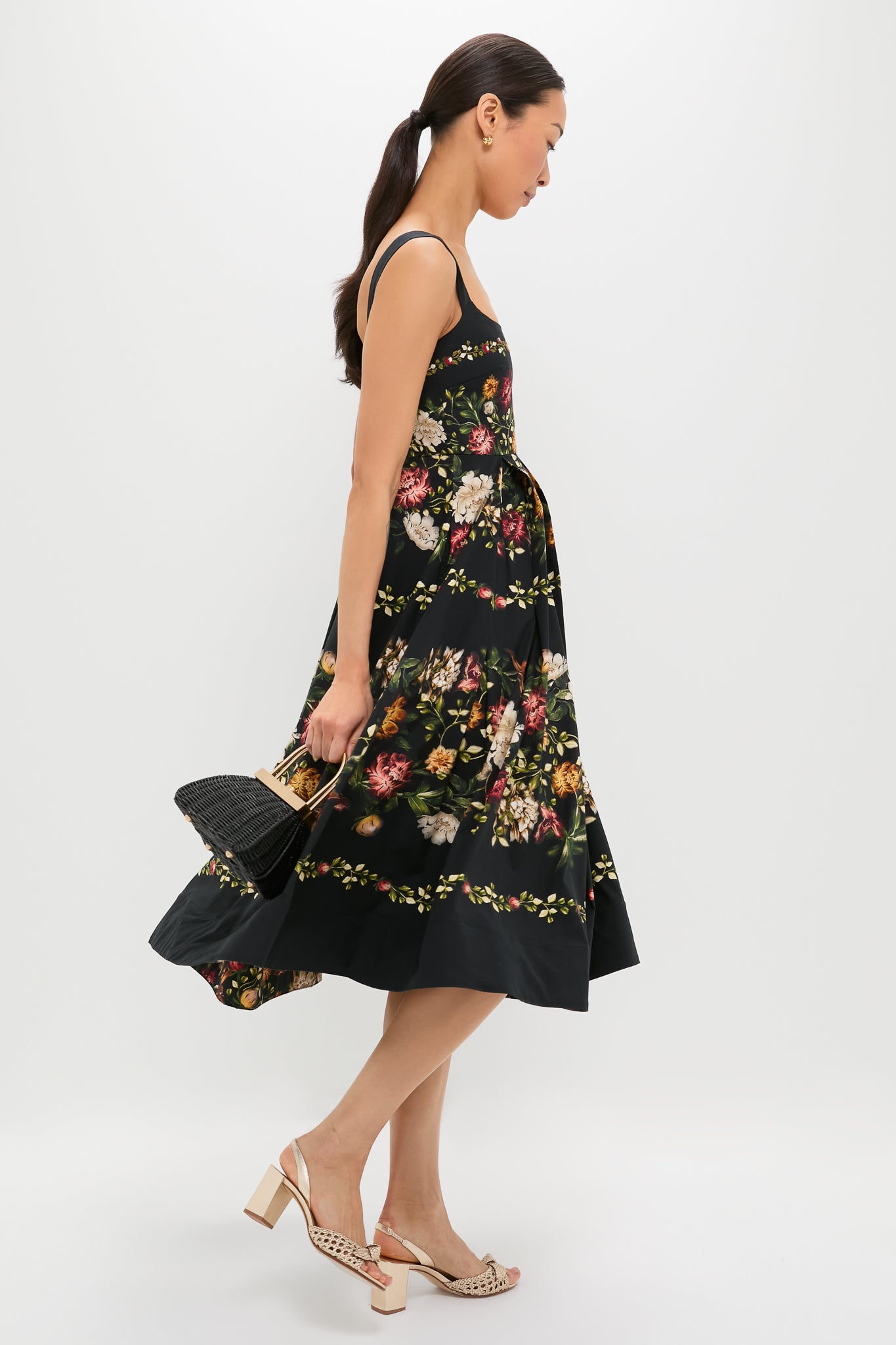 Woman wearing the classic Paramo Alcaparra Midi Dress with multicolored floral print, paired with a black wicker handbag and block-heeled sandals, exuding effortless, high-end style.