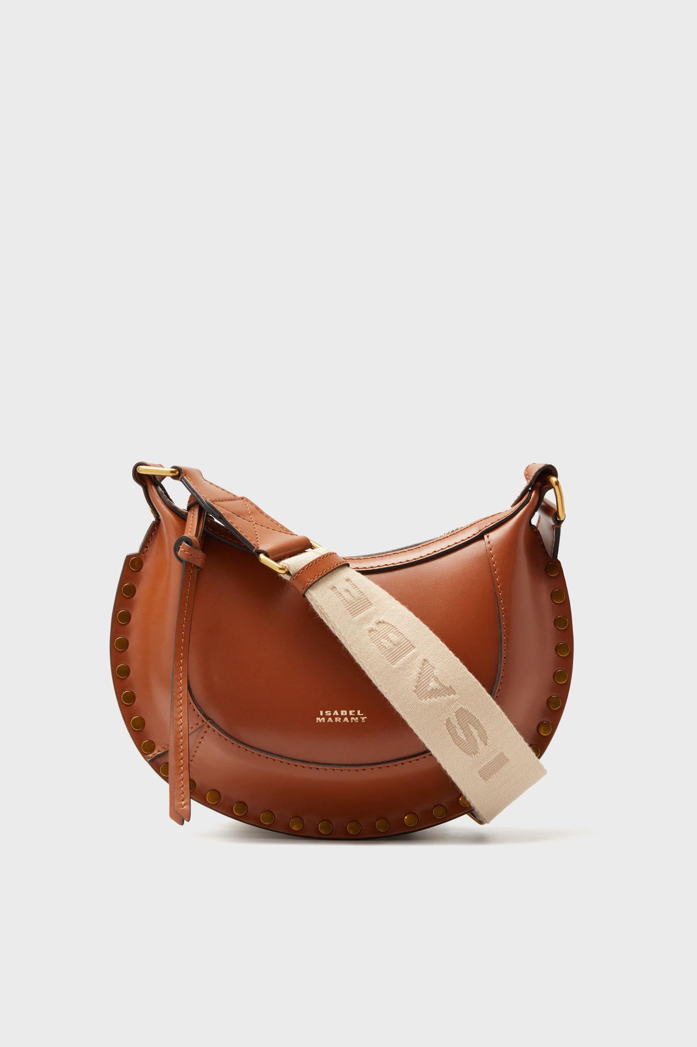A Cognac Leather Mini Moon Crossbody bag by Isabel Marant with gold rivet accents and a wide beige strap featuring the brand name, crafted from premium calfskin leather.
