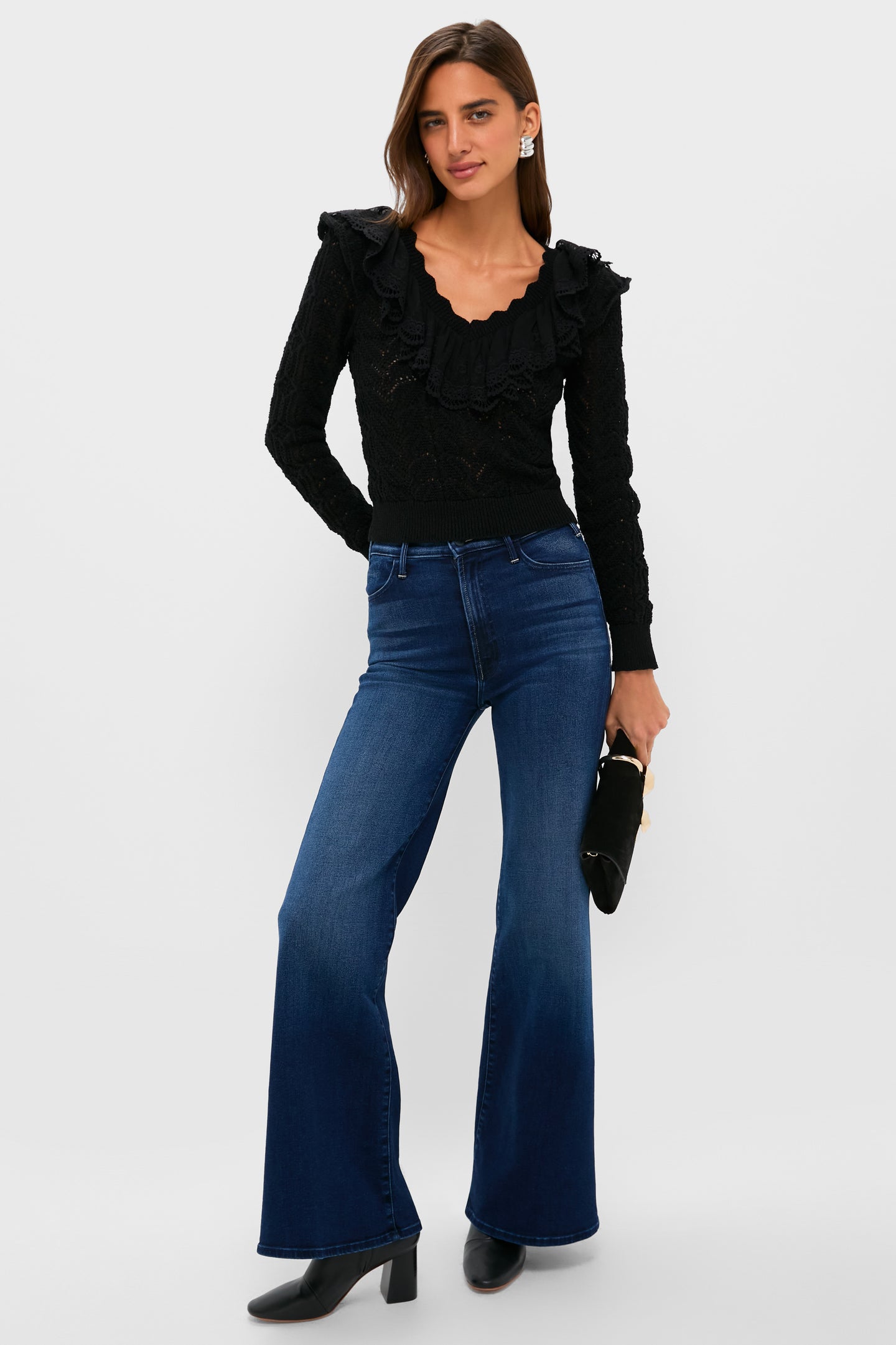 Woman wearing Black Pointelle Knit Sherry Top with ruffled V-neck, flared jeans, and ankle boots, holding a black clutch, embodying classic, effortless style.