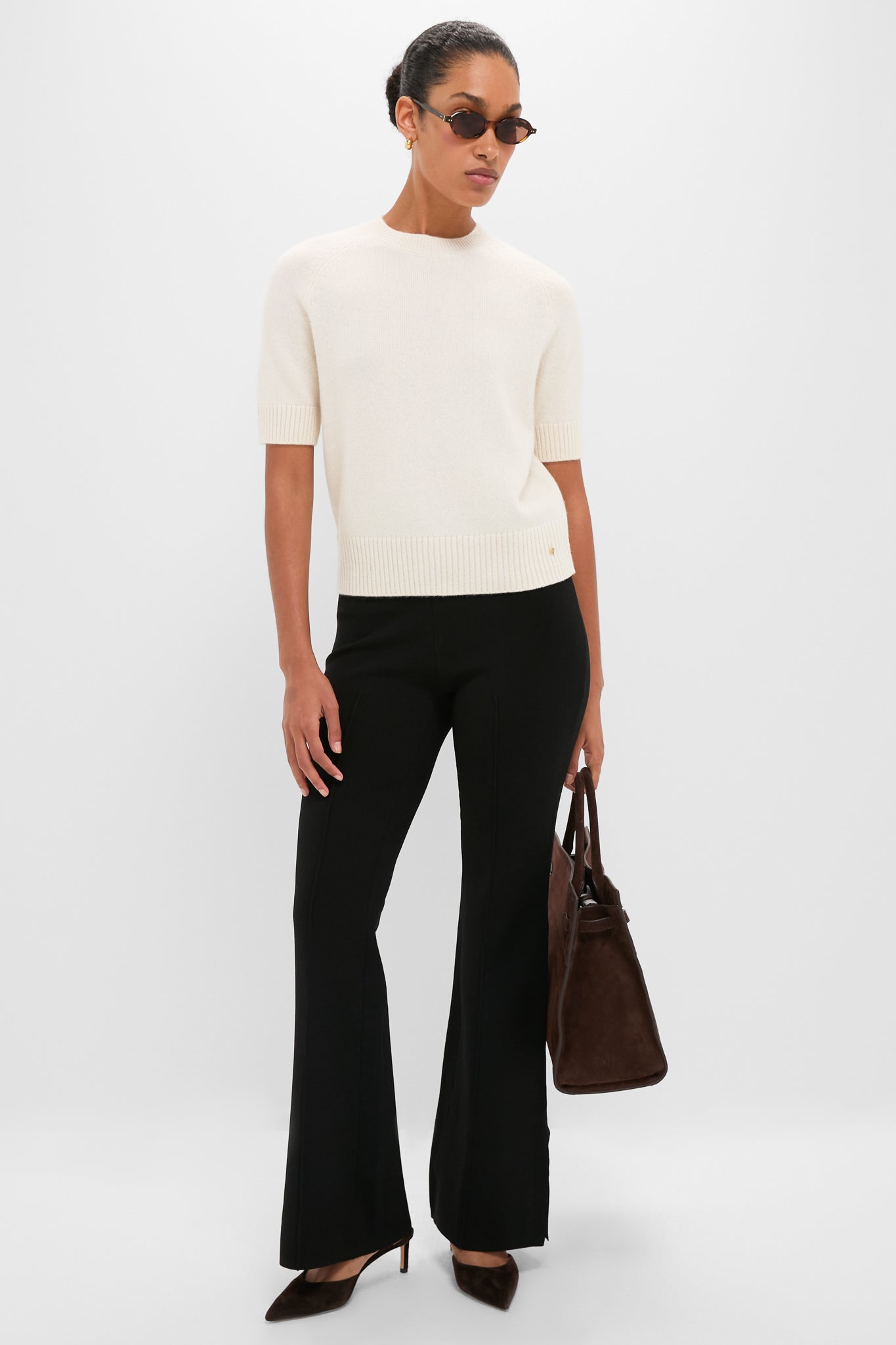 Woman modeling the Ivory Jackson Sweater, a classic, effortless high-end cashmere top with short sleeves, paired with black trousers and brown suede accessories, exuding fun sophistication.