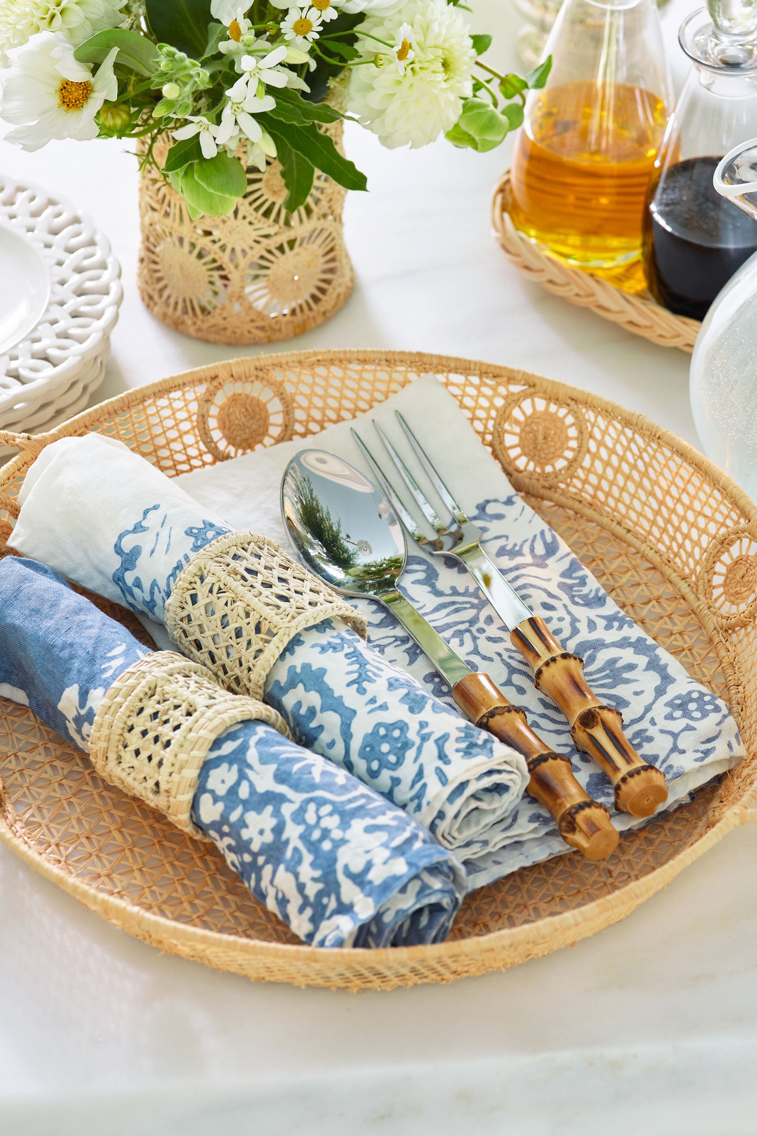 Effortlessly styled Raffia Round Tray with blue-patterned napkins, bamboo-handled cutlery, and blooms, embodying a classic, high-end coastal design for a fun, versatile tabletop display.