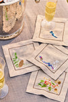 Forest Walk Cocktail Napkin Assorted Set of 4, featuring hand-embroidered woodland motifs, elegantly arranged with champagne flutes and an ice bucket, epitomizing classic, effortless, high-end table decor.