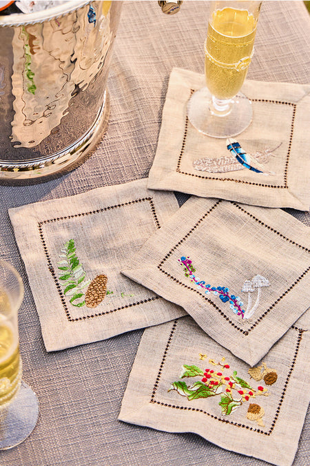 Forest Walk Cocktail Napkin Assorted Set of 4, featuring hand-embroidered woodland motifs, elegantly arranged with champagne flutes and an ice bucket, epitomizing classic, effortless, high-end table decor.