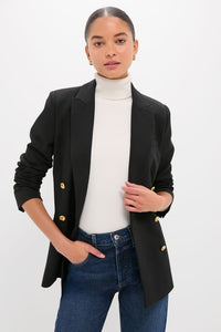 Woman wearing Black Diana Blazer with gold buttons, paired with a white turtleneck and jeans. Classic, high-end style with an effortless, fun vibe.