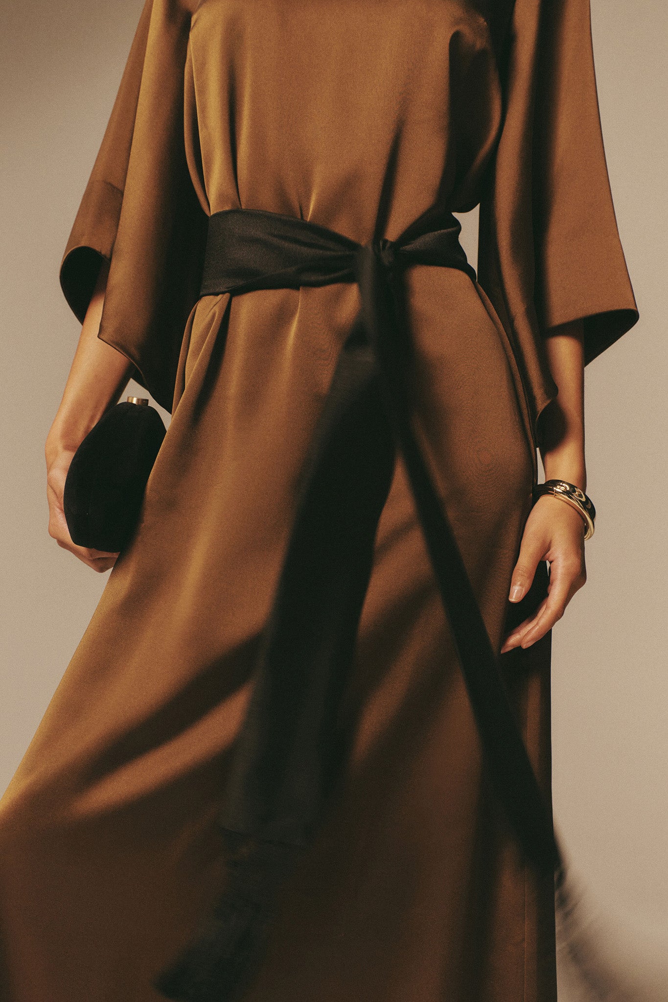 A person wears an olive-brown satin dress, showcasing the classic, high-end High Polish Gold Lennon Bangle. The bangle's effortless shine evokes a fun, sophisticated style.