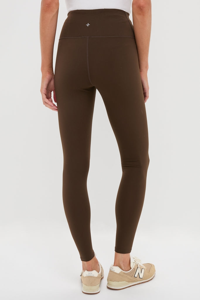 Person wearing Chocolate Brown High Rise Compression Spandex MacKenzie Legging, showcasing a classic, seamless fit with a high waistband, paired with beige New Balance sneakers.