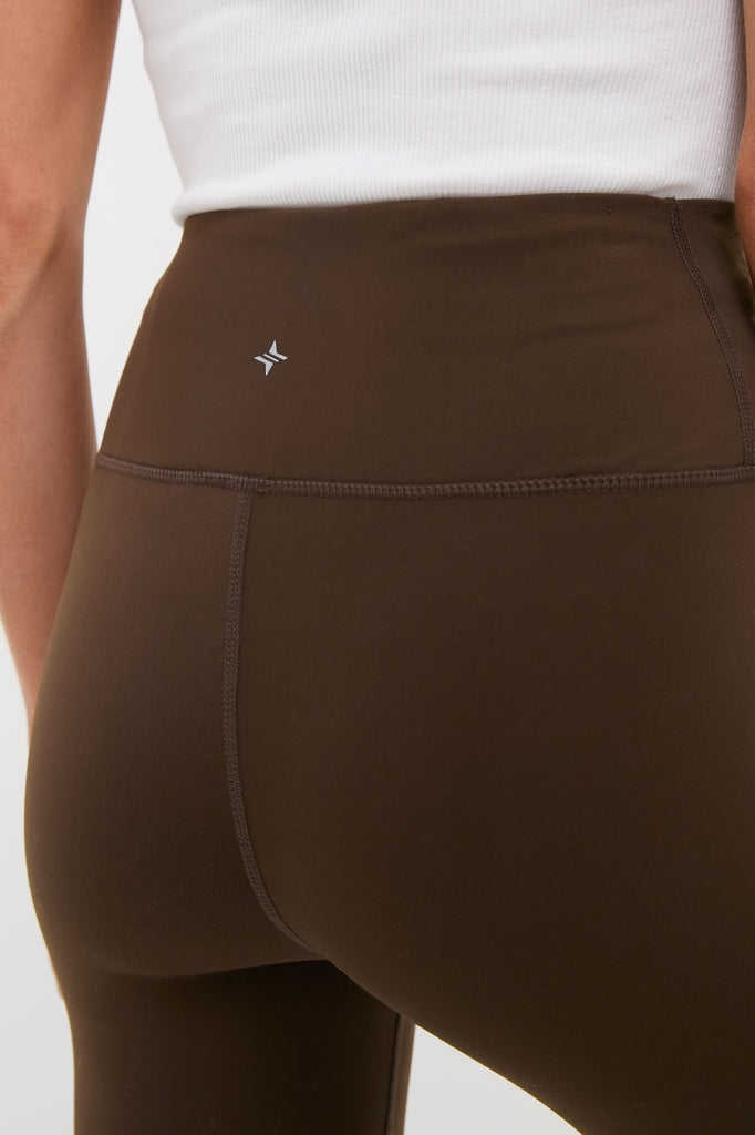 Close-up of Chocolate Brown High Rise Compression Spandex MacKenzie Legging with seamless design, reflective logo, and flattering fit for an effortless, classic, high-end look.
