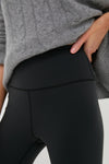 Close-up of classic Black High Rise Compression Spandex MacKenzie Legging with seamless, flattering fit, worn effortlessly with a grey cable-knit sweater, embodying fun, high-end style.
