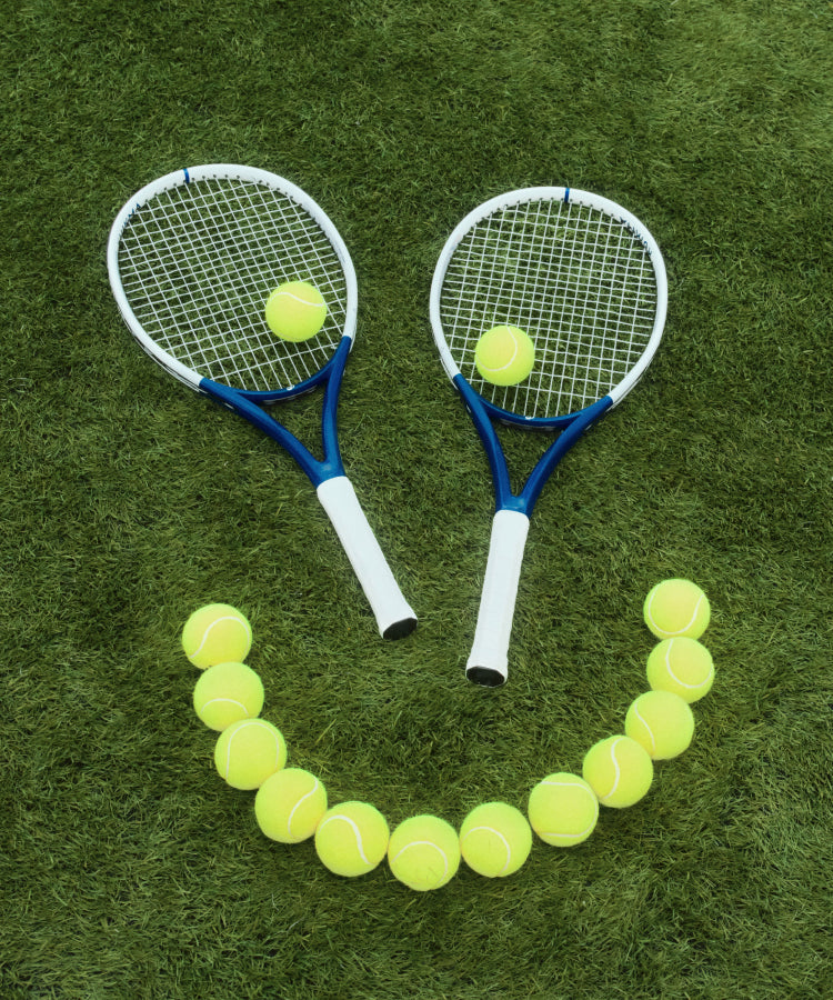 A smiley face made with tennis balls and two tennis rackets. 