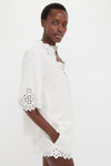 Woman modeling the classic White Shana Blouse, featuring effortless openwork embroidery and a relaxed fit, embodying a fun yet high-end style.
