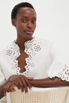 Woman wearing the classic White Shana Blouse with scalloped edges and broderie anglaise detailing, embodying effortless, high-end style, perfect for versatile, fun, and confident looks.