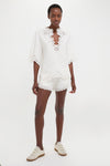 Young woman models the classic White Shana Blouse, featuring effortless openwork embroidery and a relaxed fit, paired with matching shorts and off-white sneakers for a high-end, fun look.