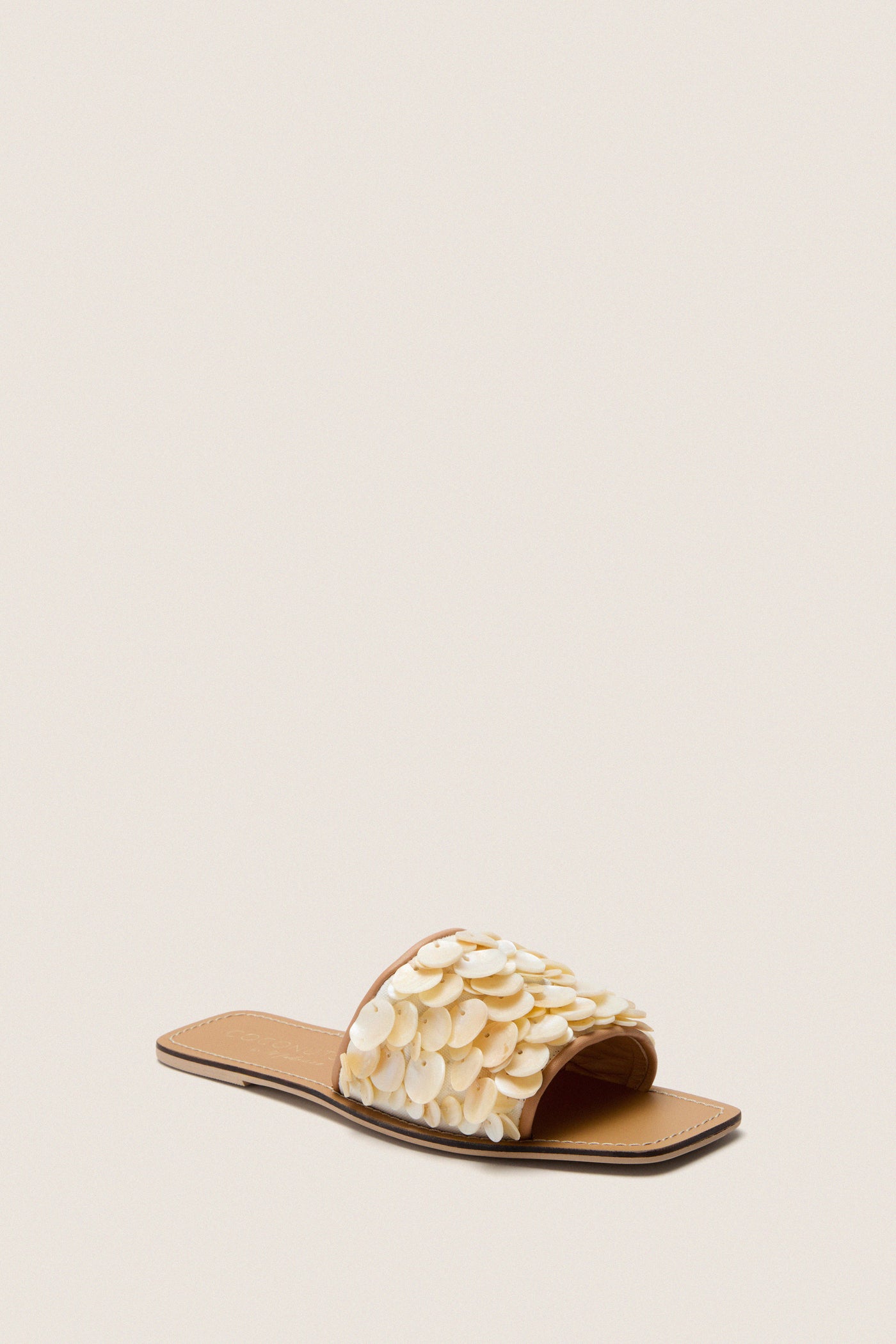 Natural Waverly Sandals feature a classic square-toed, flat design with an effortless shell-embellished upper, offering a high-end, fun beach-inspired style.