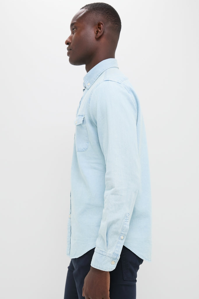 Young man in profile wearing a classic, light blue washed denim shirt and dark trousers, showcasing an effortless, fun, high-end style perfect for year-round wear.
